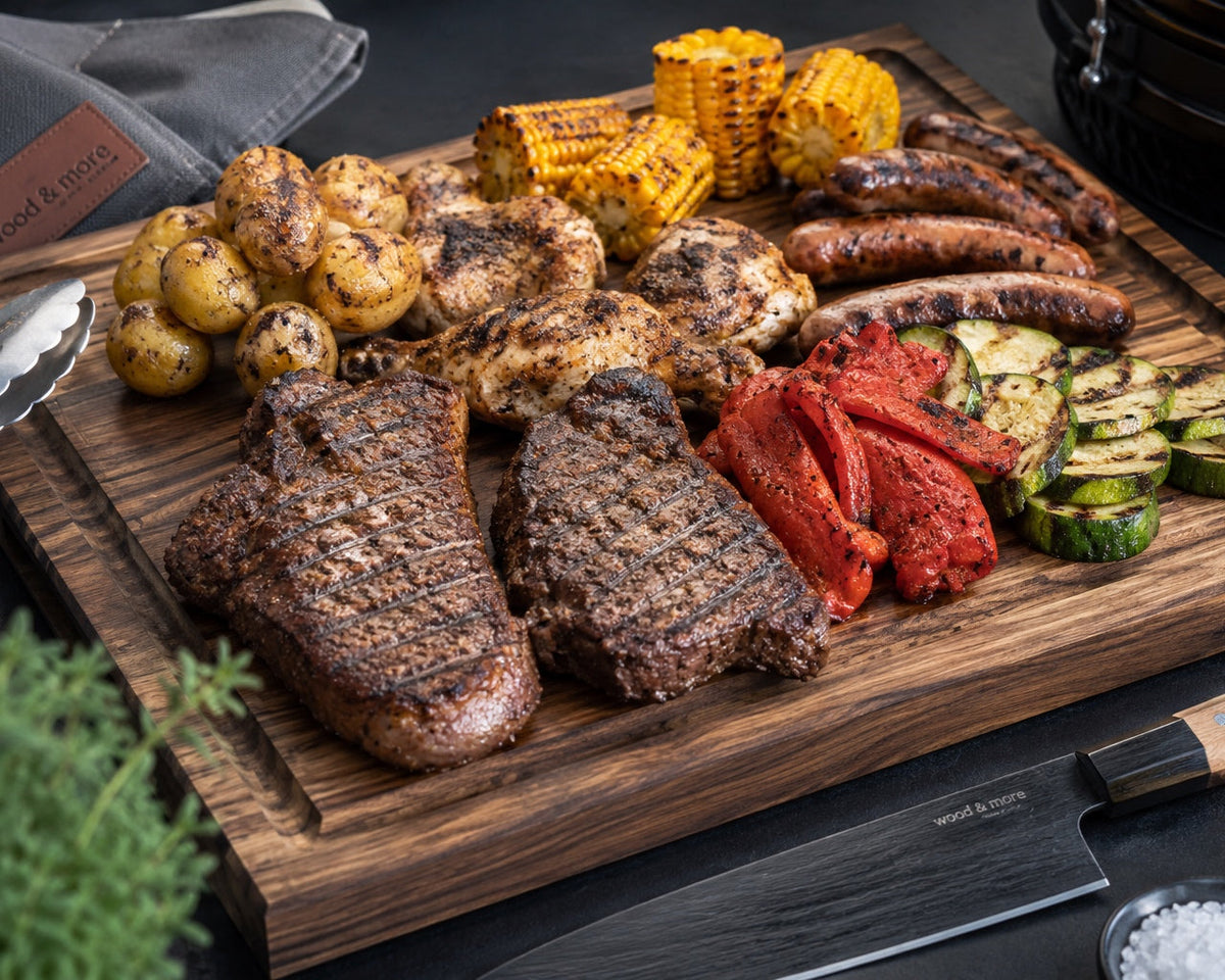 BBQ-Grillplatte mit Steak, Chicken, Würstchen, Mais, Kartoffeln und Grillgemüse auf großem Holzbrett